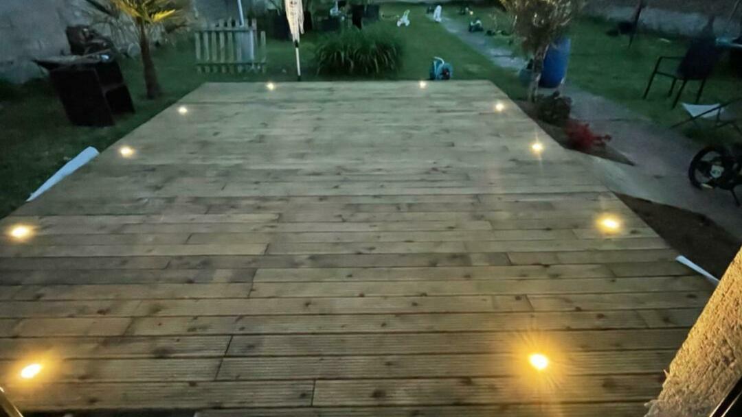Terrasse en bois avec spots d'éclairage encastrés allumés à la tombée du jour, réalisation GMCM Elec